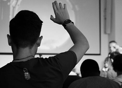 view from behind as man has hand raised in worship; stage is blurred in background